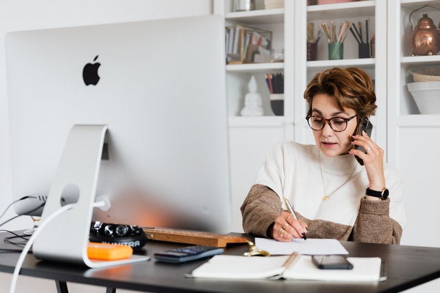 property manager on the phone while taking notes at their cluttered desk